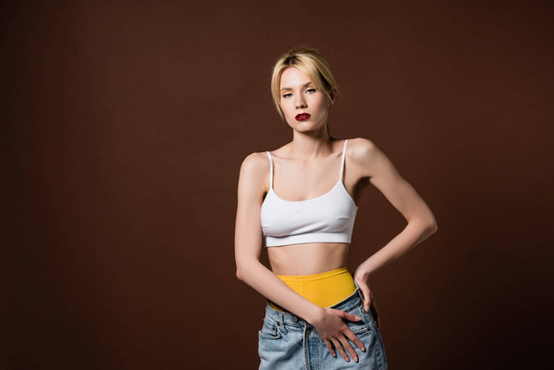 beautiful stylish blonde girl in yellow tights and jeans looking at camera isolated on brown   - 写真・画像