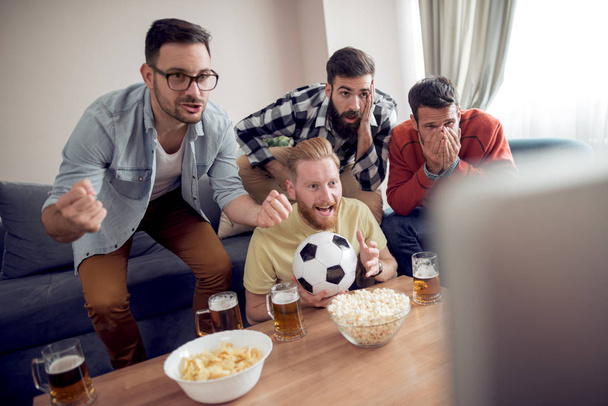 Skupina přátel, sledování fotbalového zápasu v televizi, pít pivo a jíst občerstvení - Fotografie, Obrázek