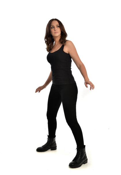 ritratto a figura intera di ragazza bruna che indossa singlet nero, jeans e stivali. posa in piedi, isolato su sfondo bianco studio
. - Foto, immagini