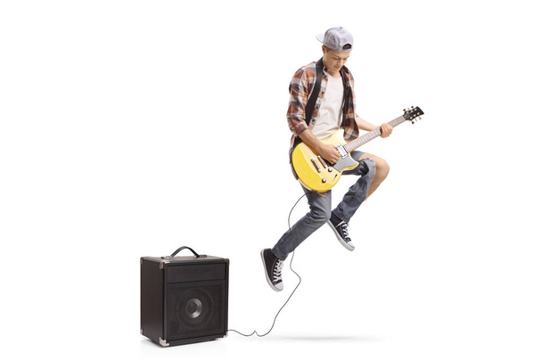 Teenage boy with an electric guitar plugged in an amplifier jumping isolated on white background - Fotó, kép
