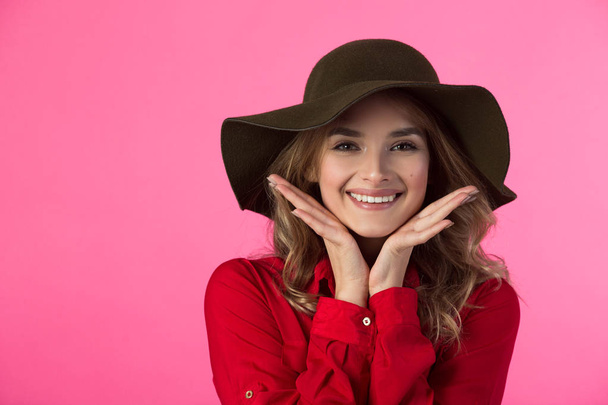 beautiful joyful young girl in a red shirt and hat on a pink background - Zdjęcie, obraz