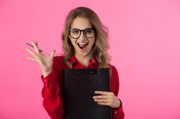 beautiful young girl in a red shirt with a folder and pen in hands on a pink background - Foto, Imagem