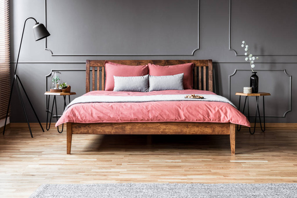 Grey and pink pillows on wooden bed in minimal bedroom interior with black lamp and molding on the wall - Foto, Bild