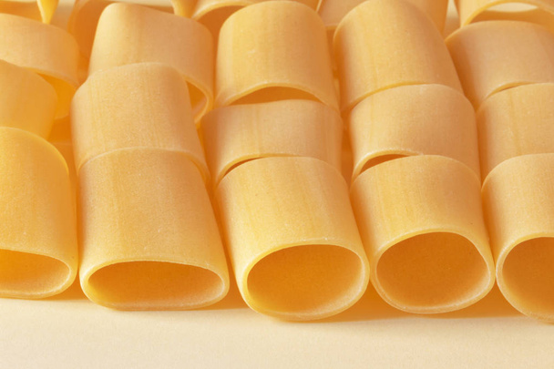 Lines of paccheri pasta on a light yellow background ,in evidence irregular pasta shapes ,horizontal composition  - Φωτογραφία, εικόνα
