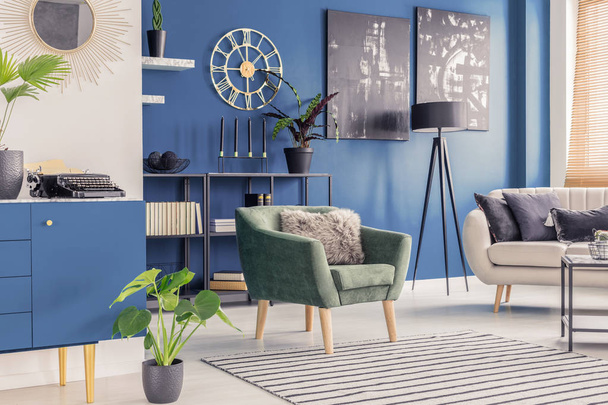 Retro typewriter and golden wall clock in a blue living room interior with paintings and modern furniture - Photo, Image