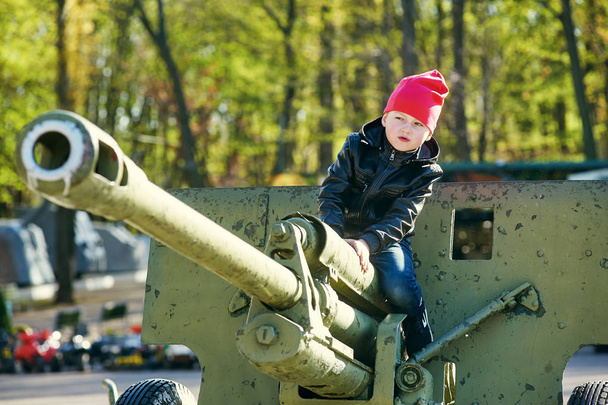 Το αγόρι παίζει με στρατιωτικό εξοπλισμό σε ένα υπαίθριο Μουσείο - Φωτογραφία, εικόνα
