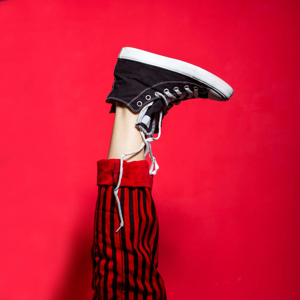 Female legs wearing striped pants and sneakers over red background. Funny woman legs - Photo, image