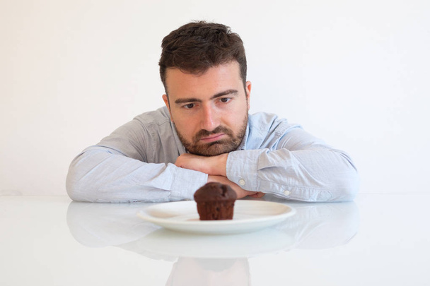 Sweet tooth man on diet tempted by chocolate muffin - Foto, Imagem