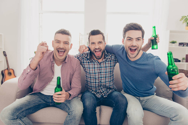 Close up portrait of attractive, stylish, cheerful guys yelling goal with wide open mouths, holding bottles with lager in hands, watching soccer word cup, cheering for favorite team - Fotoğraf, Görsel
