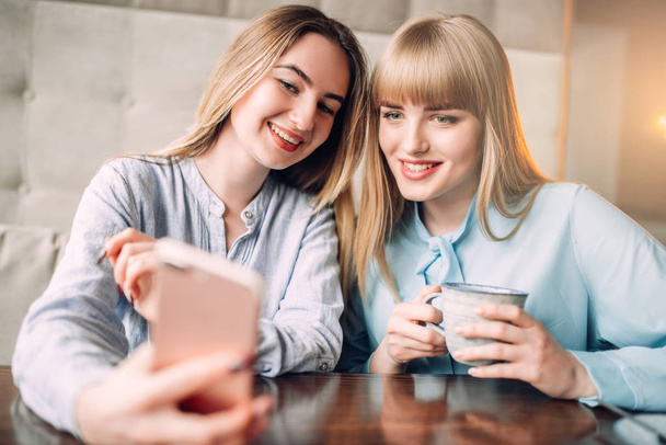 zwei glückliche Freundinnen trinken Kaffee im Café und schauen auf ihr Handy  - Foto, Bild