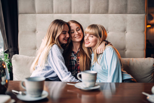τρεις ευτυχισμένος θηλυκό φίλους πίνοντας τον καφέ στην καφετέρια και να αγκαλιάζει  - Φωτογραφία, εικόνα