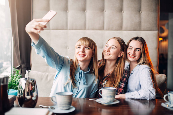 trzy szczęśliwe koleżanki picia kawy w kawiarni i biorąc selfie  - Zdjęcie, obraz
