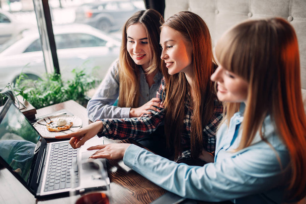 drie vriendinnen foto's kijken op laptop in café, chocoladedessert en alcohol op tafel - Foto, afbeelding