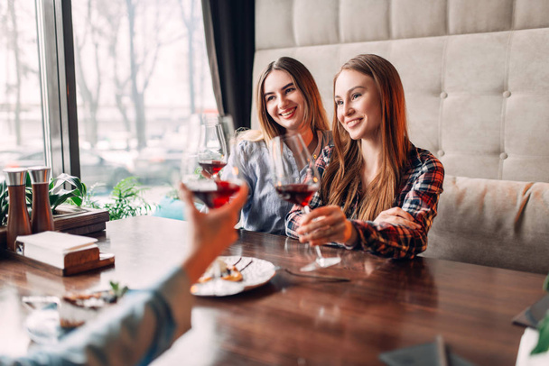 portrait of three female friends drinking red wine, young women celebrating in cafe - Photo, Image