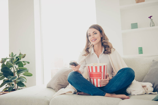 Portrait of pretty, charming, cheerful, trendy house wife with curls hairstyle cover with coverlet having popcorn in hands using console searching for interesting program - Foto, Imagen