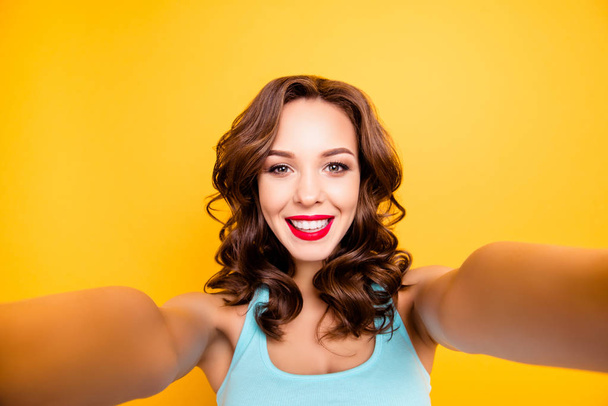 Self portrait of trendy charming girl with modern hairdo shooting selfie on front camera isolated on yellow background - Фото, изображение