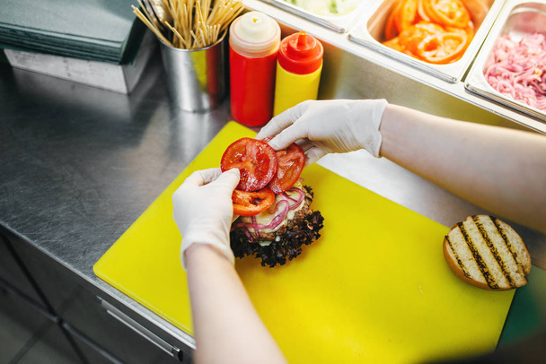мужчина повар в перчатках на работе, процесс приготовления гамбургеров
 - Фото, изображение