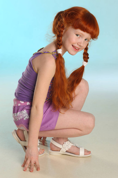 Beautiful charming little redhead girl demonstrates her summer clothes squatting. Happy attractive child with a slender body and slim bare legs. Fashion pre-teen model 8 years old. - Φωτογραφία, εικόνα