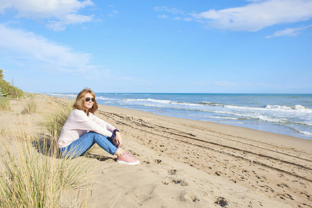 Full length shot of middle aged woman sitting  at the beach and relaxing.  - Fotografie, Obrázek