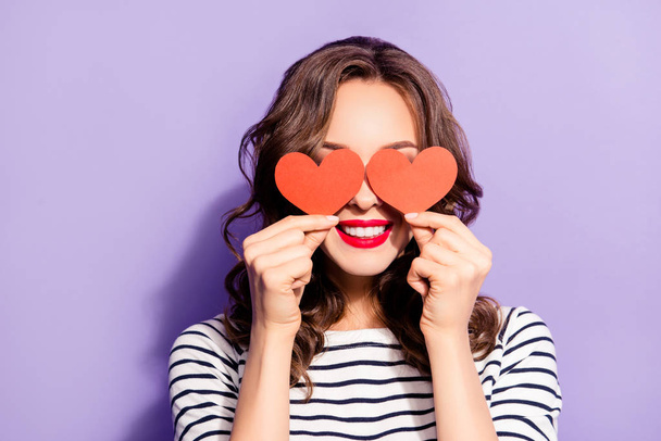 Portrait of lovely creative girl with white teeth red pomade covering closing eyes with two carton paper small little heart figures love signs isolated on violet background - Foto, Imagen