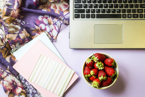 春職場のラップトップ、ノートブック、紫色の背景にイチゴのボウル。平面図、平面レイアウト - 写真・画像