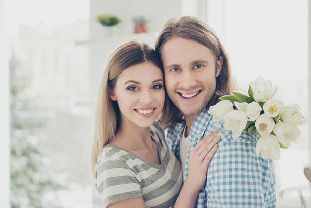 Portrait of cheerful positive couple enjoying holiday together charming woman with handsome man holding bouquet of white tulips in hand looking at camera. Love story true feeling concept - Zdjęcie, obraz