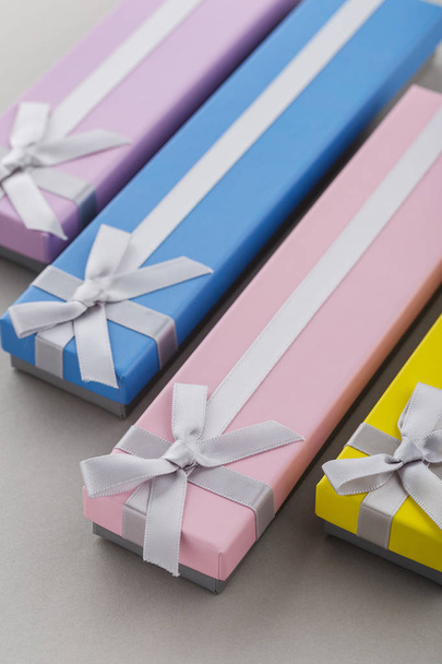 Colorful present boxes with ribbon bows on gray background. Pink, yellow, blue and violet long gift boxes for holiday presents - Photo, Image