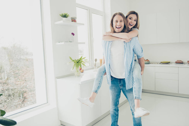 Love story! Portrait of funky trendy partners kidding in modern kitchen with interior, handsome man carrying on back lover looking at camera - Valokuva, kuva