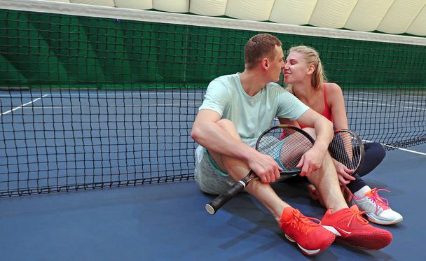 jeune homme et femme s'embrassent assis sur un court de tennis près du filet de tennis
 - Photo, image