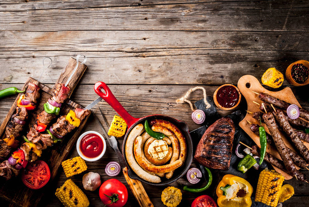 Assortment various barbecue food grill meat, bbq party fest - shish kebab, sausages, grilled meat fillet, fresh vegetables, sauces, spices, on old wooden rustic table, above copy space - Photo, Image