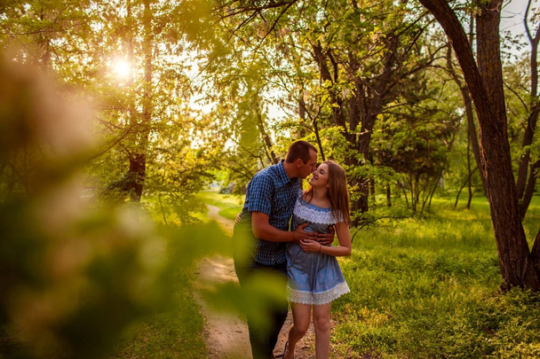 Onnellinen pari kävelemässä kevätmetsässä. Nuori mies ja tyttö halaavat ja suutelevat auringonlaskun aikaan
. - Valokuva, kuva