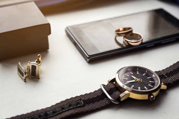 Different men's accessories such as: cufflinks, watches,  rings and phone - are on the table - 写真・画像