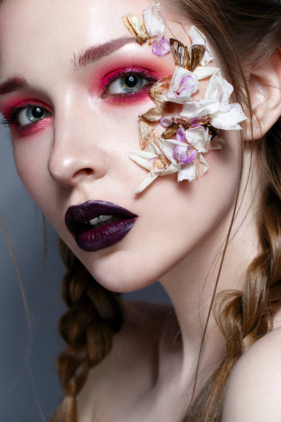 Young girl with bright pink creative make-up. Beautiful model with lips of the color of Marsala and application of flowers. Suspended flowers and beetles. Beauty of the face. Photo taken in the studio - Foto, immagini