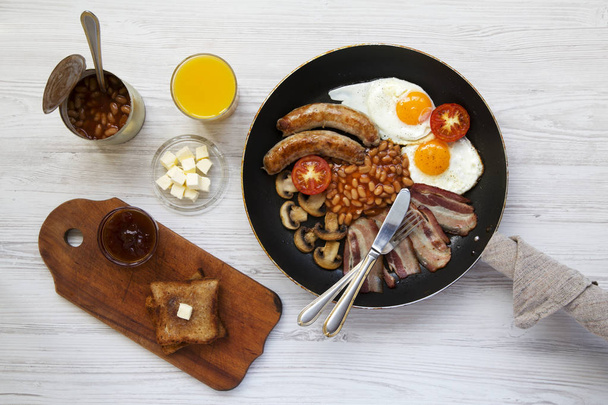 Англійський сніданок у сковороді з Смажені яйця, бекон, сосиски, боби і тости на білому тлі дерев'яні, вид зверху. З плоским лежав. Зверху. - Фото, зображення