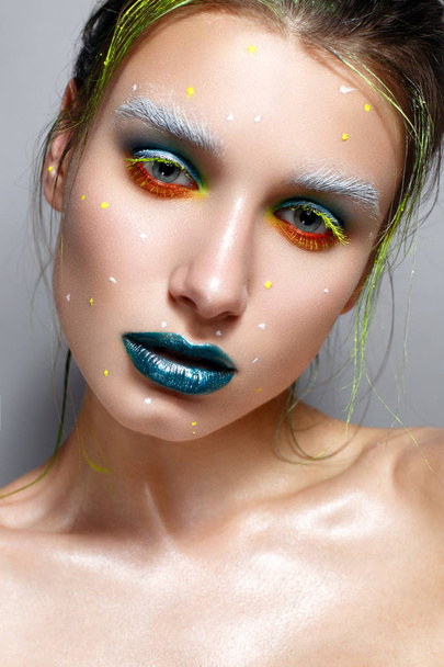 Young girl with creative multi-colored make-up. Bright neon colors. Turquoise lips and shining skin. The cosmic image. Beauty of the face. Photo is taken in the studio. - Foto, Imagem