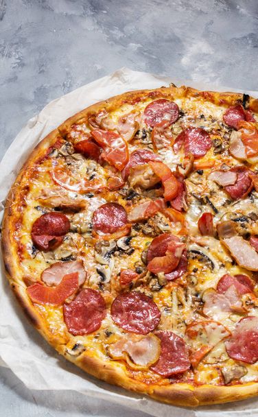 Pizza casera fresca con pepperoni, jamón, queso y salsa de tomate sobre fondo de hormigón rústico
. - Foto, imagen