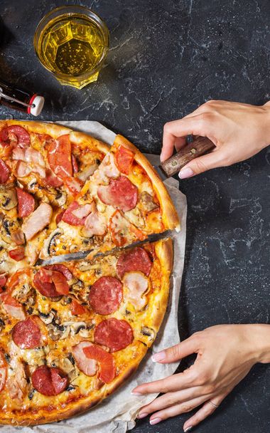 Las manos femeninas sostienen un pedazo de pizza casera fresca con pepperoni, jamón, queso sobre fondo de piedra rústica. Vista superior
 - Foto, Imagen