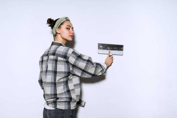 a young girl in a plaid shirt leveling a wall with a spatula, doing repairs in the apartment - Фото, зображення