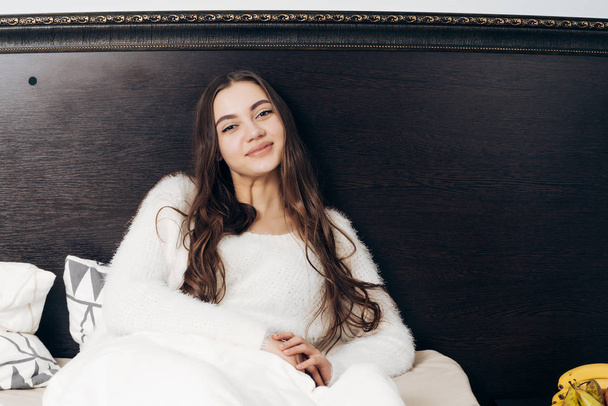 hermosa chica de pelo largo en pijama blanco se encuentra en la cama, descansando después del día de trabajo
 - Foto, imagen