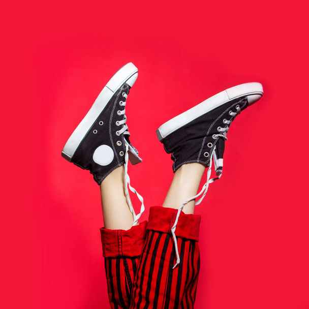 Female legs wearing striped pants and sneakers over red background. Funny woman legs - Фото, зображення