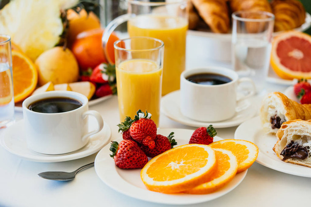 Healthy breakfast served with black coffee, croissant, orange juice and fruits - Fotó, kép