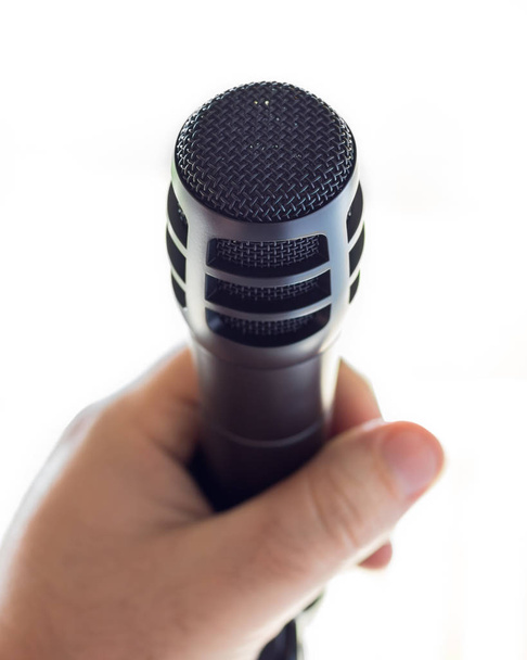 A sleek black microphone on a stand in front of open white space. The hand of a white male is holding the microphone. - Foto, Bild