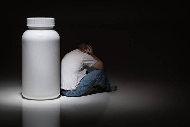 Man Holding Head Sitting Next To Blank Medication Bottle. - Zdjęcie, obraz