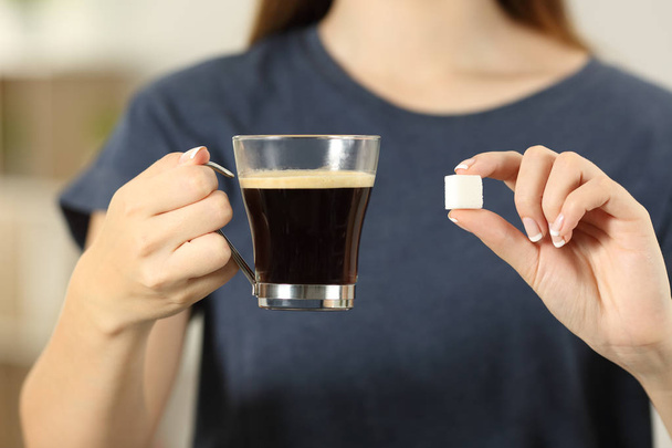 Front view close up of a woman hands holding coffee cup and a sugar cube at home - Photo, image
