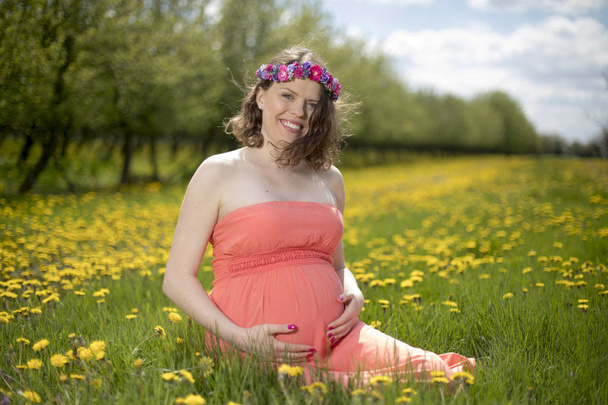 Krásná těhotná žena v jarní zahradě mezi rozkvetlé pampelišky - Fotografie, Obrázek