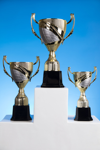 Copas de premios ganadores en podio blanco, fondo deportivo
 - Foto, imagen