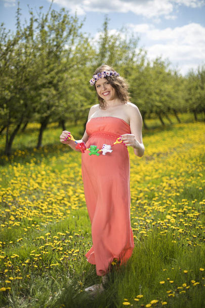 Όμορφη έγκυος γυναίκα στον κήπο την άνοιξη ανάμεσα σε ανθισμένα πικραλίδες - Φωτογραφία, εικόνα