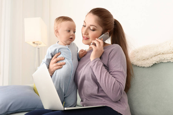 Young mother holding baby while working at home - Photo, Image