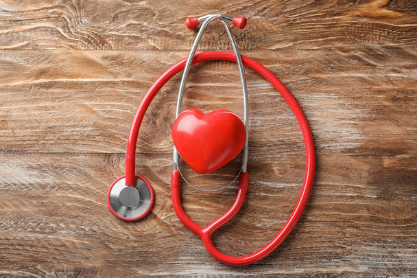 Stethoskop mit rotem Herz auf hölzernem Hintergrund. Gesundheitskonzept - Foto, Bild