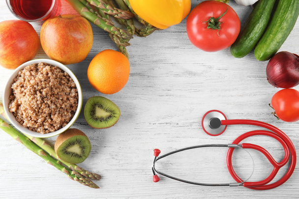 Frame made with stethoscope, fresh fruits and vegetables on wooden background. Healthy food concept - Photo, Image